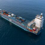Home A drone captures a vibrant container ship navigating deep blue ocean waters.